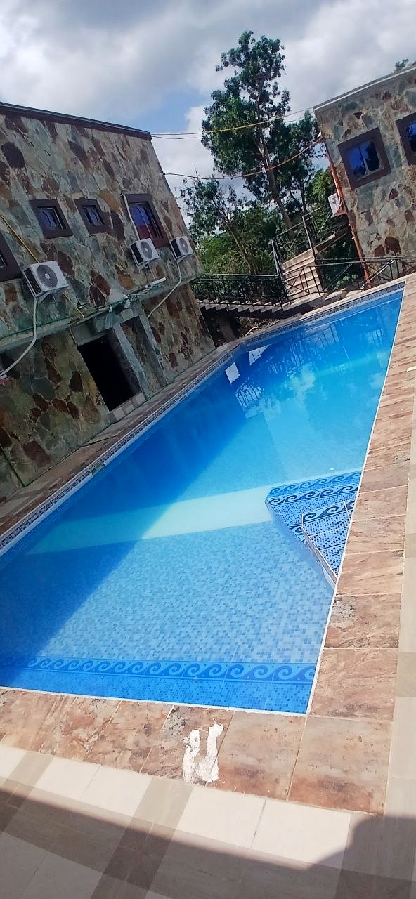 Blue swimming pool bordered by tiled decking and guest-house buildings.